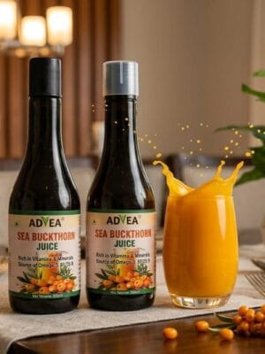 Two bottles of Advea Sea Buckthorn Juice on a dining table next to a splashing glass of orange juice, a lit candle, and fresh sea buckthorn berries.