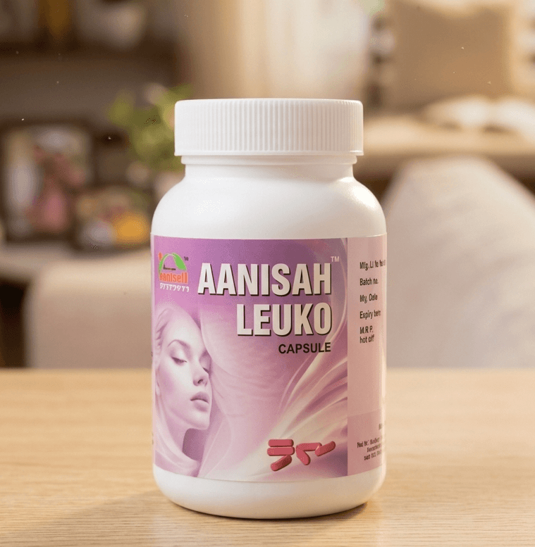 A photograph of a white bottle containing Aanisah Leuko capsules for female health, with a pink label featuring an illustration of a woman's face. The bottle is placed on a light wooden table against a blurred background of a living room with plants and a window.
